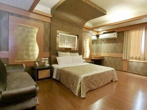 Un dormitorio amplio con una cama grande, una mesita de noche, una silla y un aire acondicionado de pared.