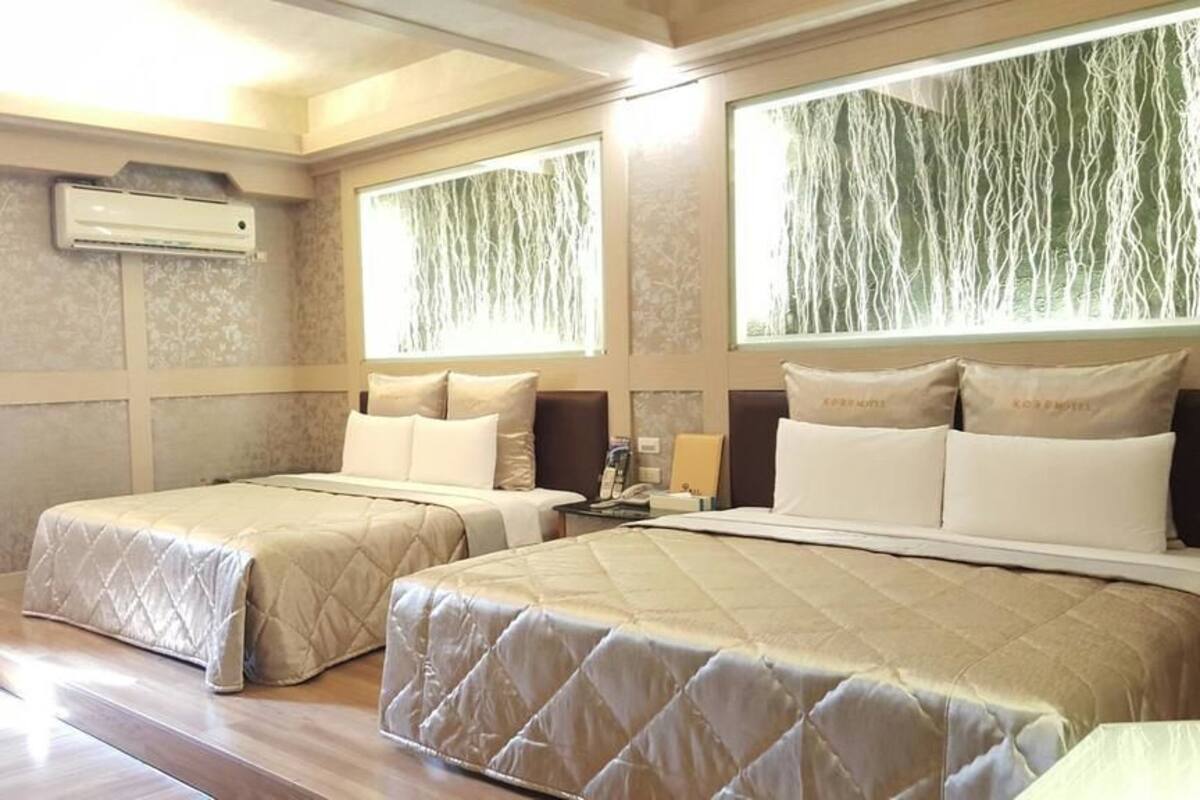 A hotel room with two beds, a large window with a view, and an air conditioning unit on the wall.