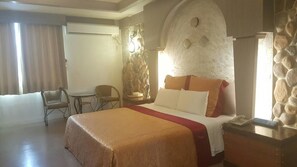 A hotel room with a large bed, a desk, a chair, and a stone wall. - Wind Coast Motel (Hsinchu)