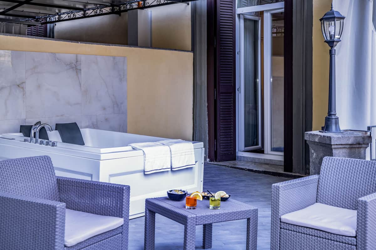 A spa area with a large bathtub, wicker chairs, and a small table with drinks.