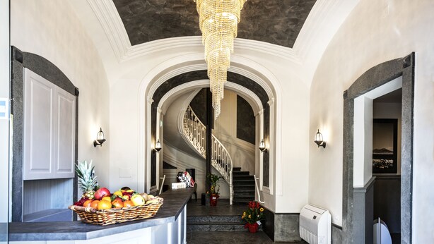 A grand hallway with a chandelier, a fruit basket, and a staircase leading to a lower level. - Villa Elisio Hotel & Spa (Naples)