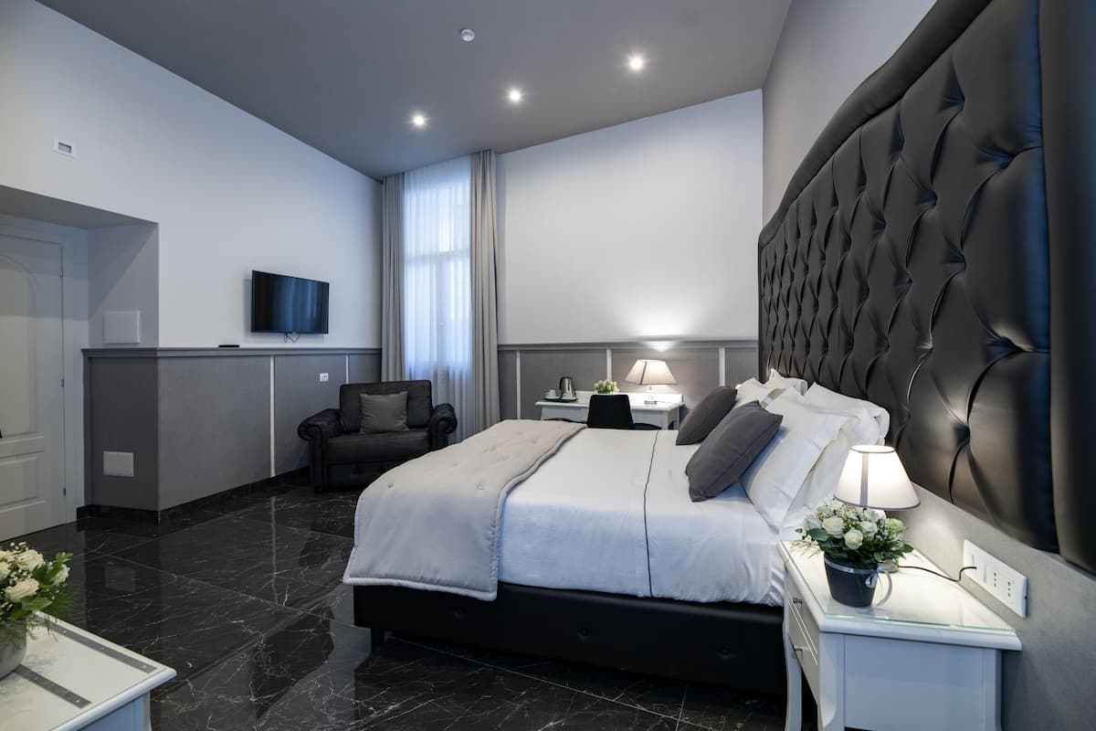 A modern bedroom with a large bed, a bedside table with a lamp, a TV mounted on the wall, and a chair.