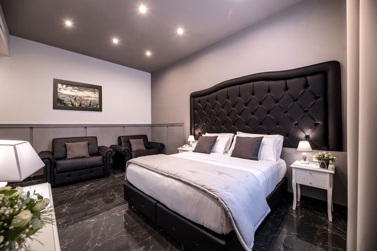 A modern bedroom with a large bed, two sofas, a nightstand, and a framed picture on the wall.