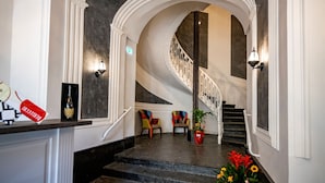 A grand staircase with a marble floor, white walls, and a chandelier. There are colorful chairs and a potted plant at the bottom of the stairs. - Villa Elisio Hotel & Spa (Naples)