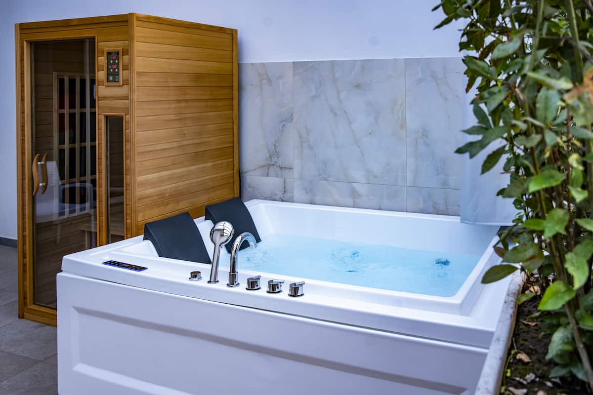 A spa room with a white bathtub, wooden sauna, and marble walls.