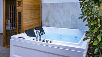 Una stanza spa con una vasca da bagno bianca, una sauna in legno e pareti in marmo.