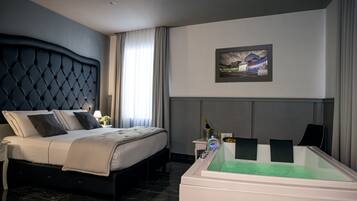 A modern hotel room with a large bed, a bedside table with a lamp, a framed picture on the wall, and a green-tinted bathtub.