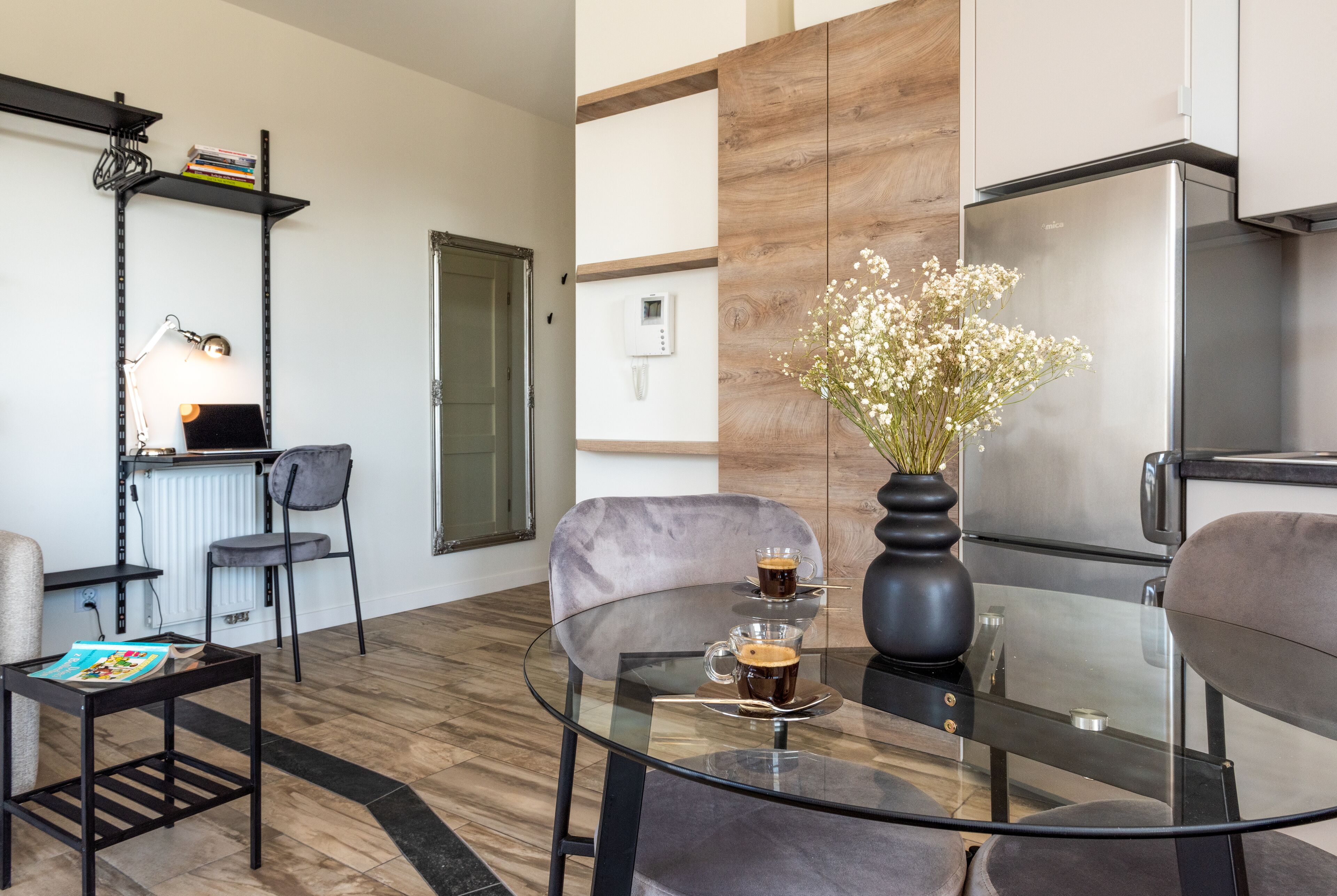 Una sala de estar moderna con una mesa de centro de vidrio, dos sillones, una estantería, un radiador y un refrigerador.