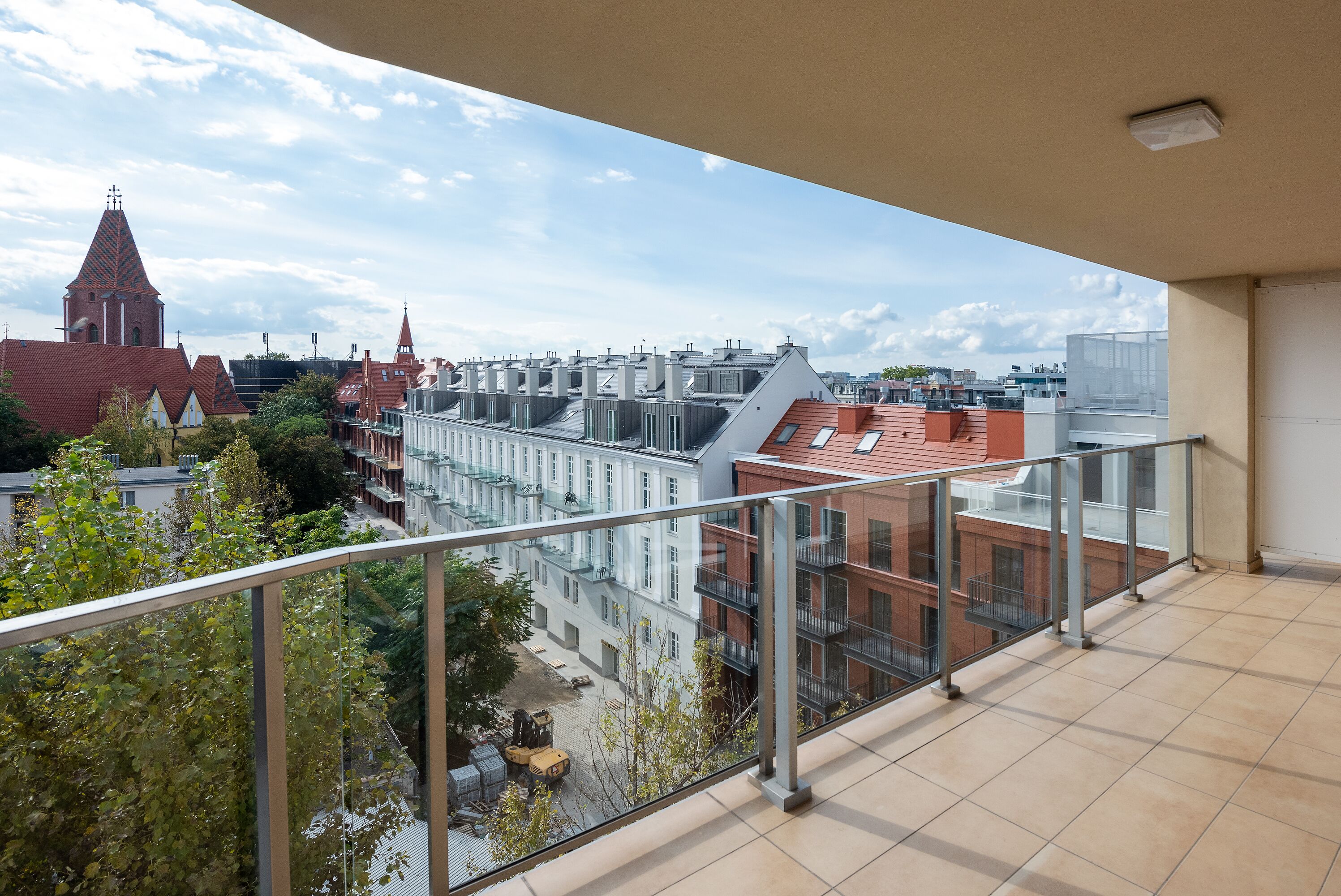 A balcony with a view of a cityscape, including a church tower and residential buildings.