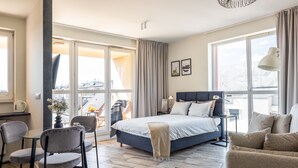 A modern hotel room with a large bed, a desk, a chair, and a sofa.