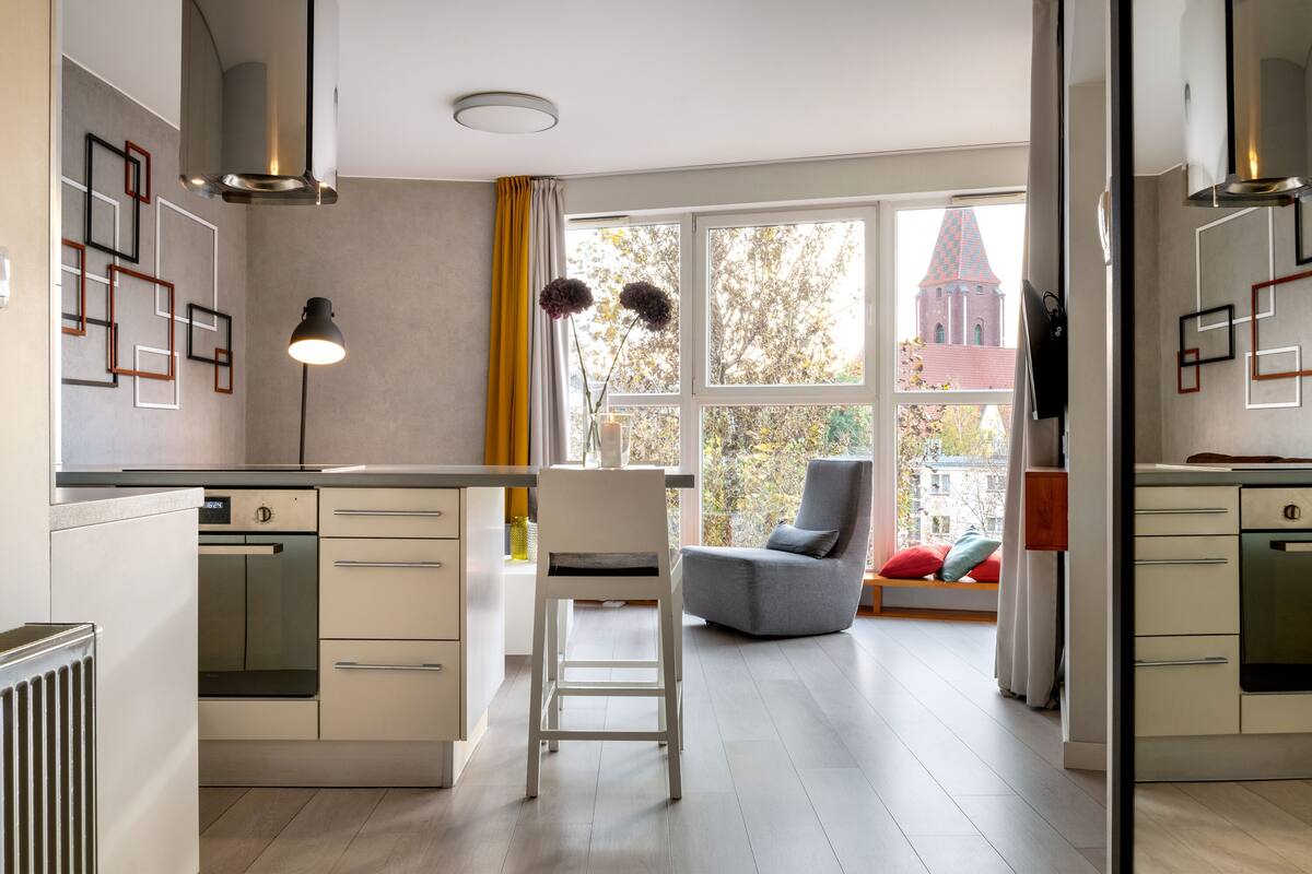 Eine moderne Küche mit einer zentralen Kochinsel, einem Essbereich mit einem grauen Stuhl und Blick auf ein Gebäude.