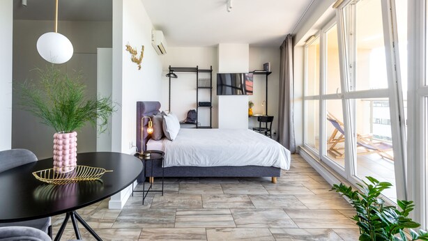 A modern bedroom with a bed, bedside tables, a TV, and large windows.