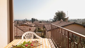 A balcony with a table set for dining, overlooking a town with terracotta rooftops and a clear sky. - Appartamento Anna (San Felice del Benaco)