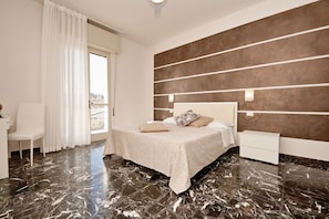 A modern bedroom with a bed, nightstands, a chair, and a large window with curtains. - Appartamento Anna (San Felice del Benaco)