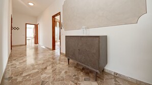 A hallway with a stone floor, a grey cabinet, and a large white wall. - Appartamento Anna (San Felice del Benaco)