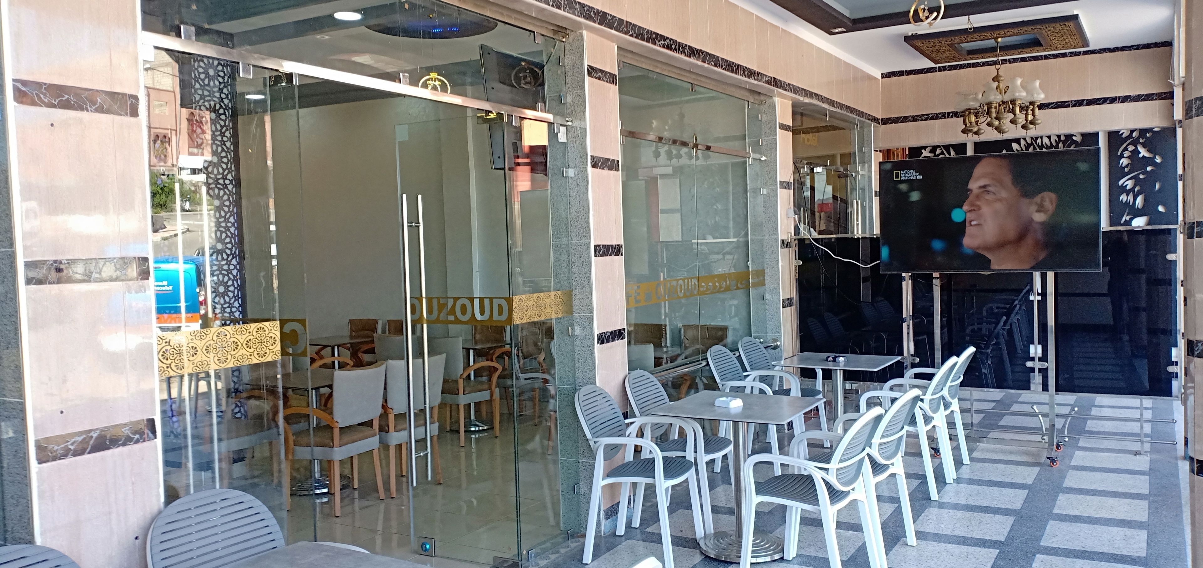 A restaurant with glass walls, outdoor seating, and a television screen.