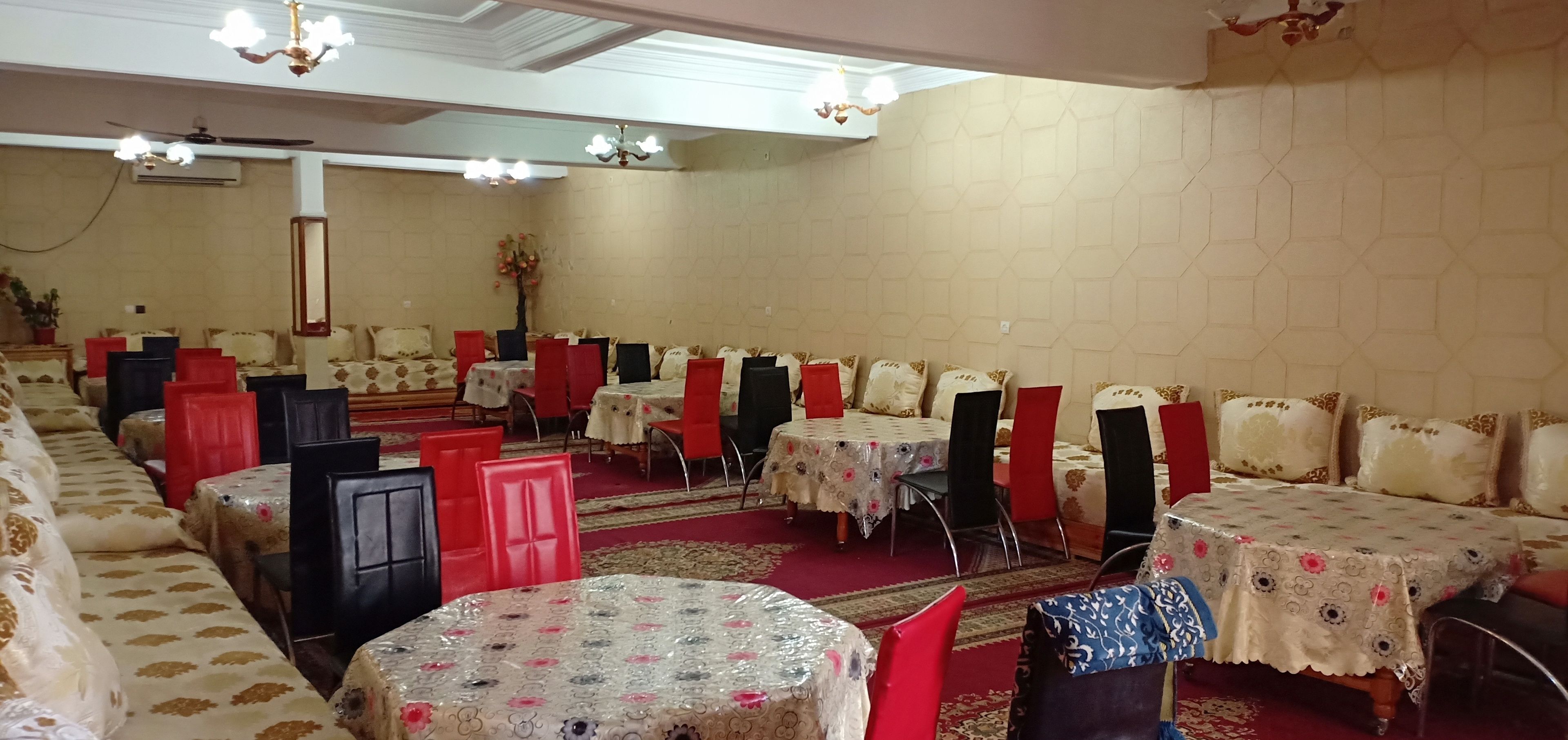 A banquet hall with multiple round tables, red and black chairs, and a red carpet.