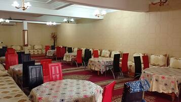 A banquet hall with multiple round tables, red and black chairs, and a red carpet.