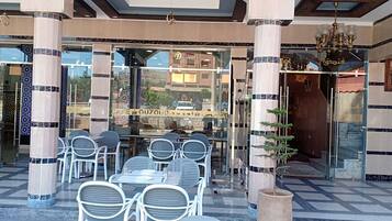 A hotel entrance with a glass facade, outdoor seating area, and a sign reading "CAFE GUZOUD".