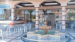 Un vestíbulo de hotel con una fuente central, sillas blancas y un mostrador de recepción.