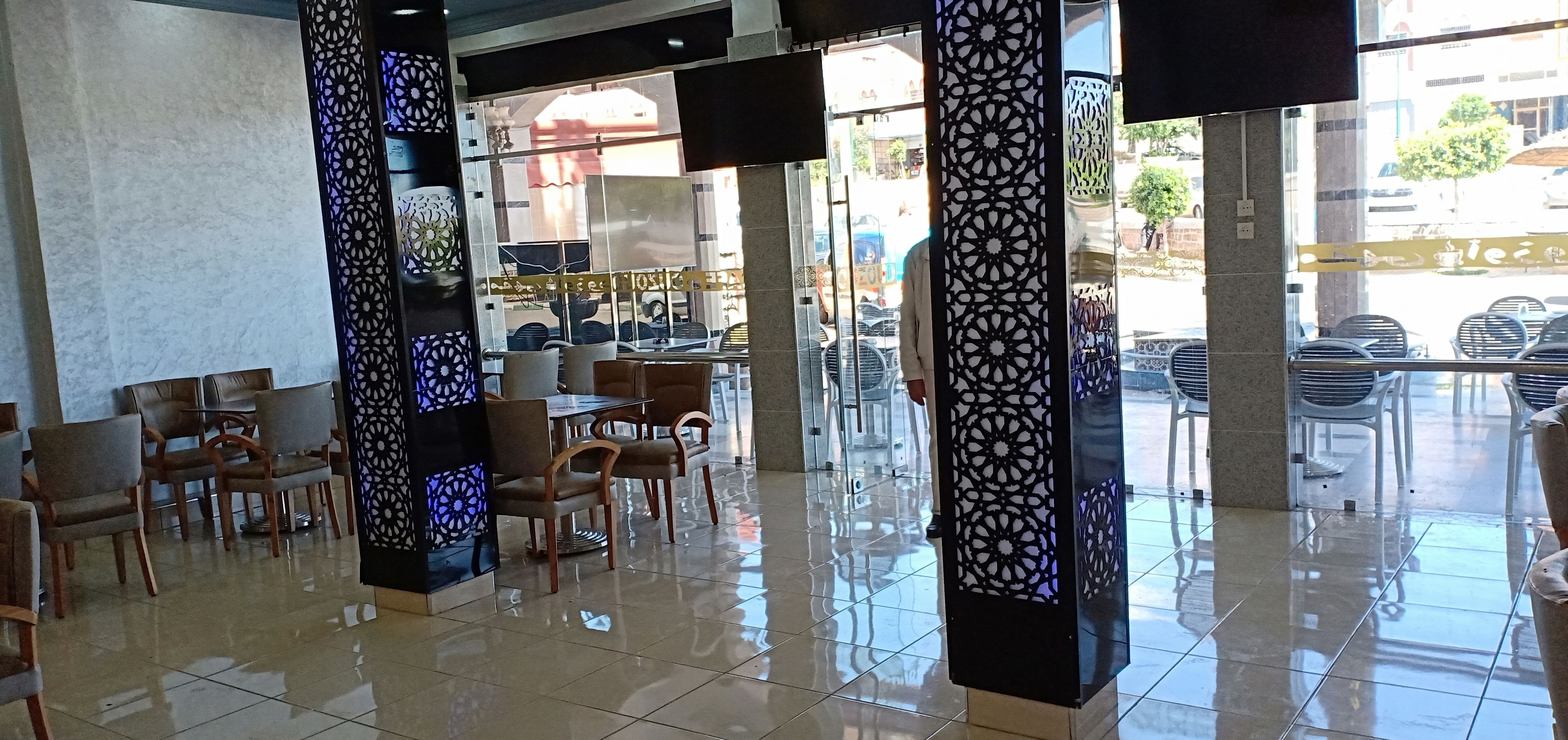 A spacious indoor area with tiled flooring, multiple seating arrangements including tables and chairs, and decorative pillars with intricate patterns.