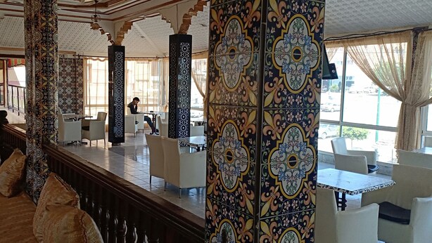 Un interior tradicional con columnas decoradas, una zona de estar con sofás y mesas, y vistas al exterior.