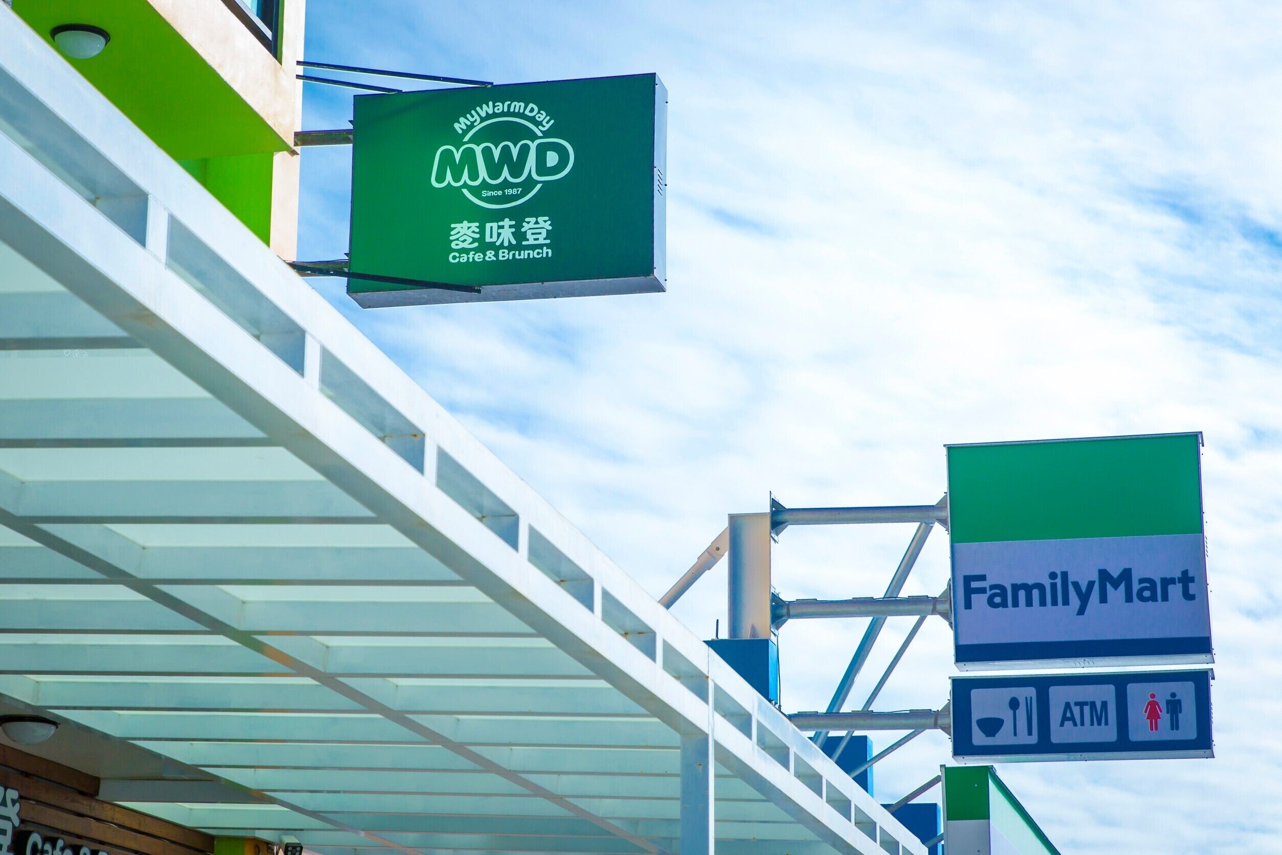 A commercial building with a green sign for MyWarmDay Cafe & Brunch and a FamilyMart sign with an ATM symbol.