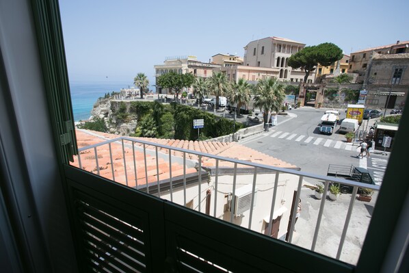 A balcony with a view of a coastal town, including buildings, a road, and a clear sky.