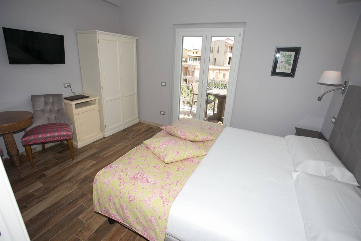 A bedroom with a bed, a chair, a desk, a wardrobe, and a TV.
