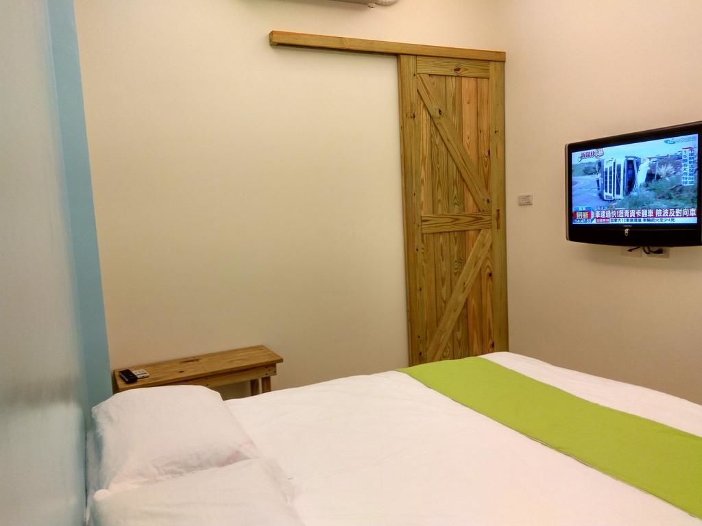 Quarto com cama, guarda-roupa de madeira, televisão na parede e uma pequena mesa de madeira.