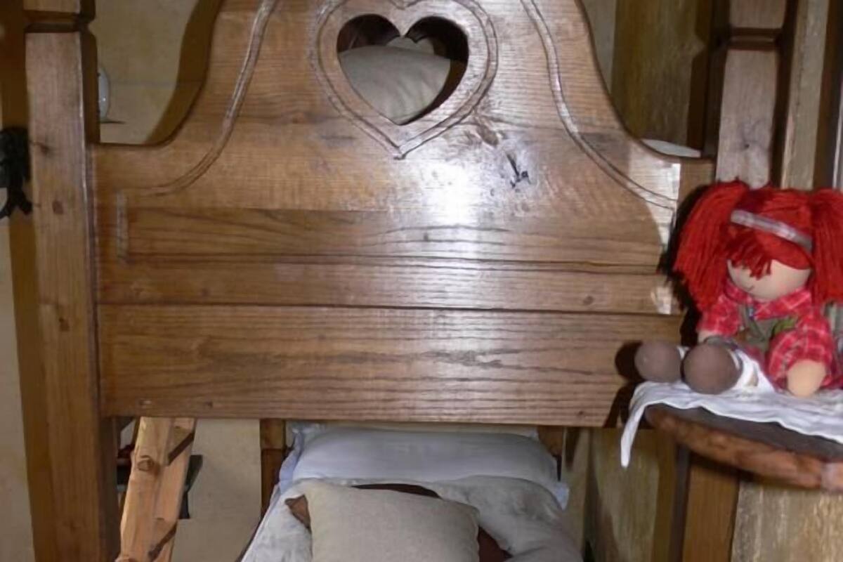 A wooden bunk bed with a heart-shaped cutout on the headboard, a small shelf with a doll, and a bedside table with a checkered cloth.