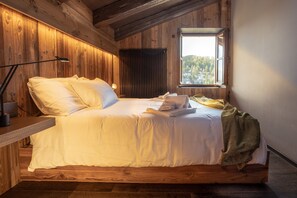 A wooden cabin bedroom with a bed, a nightstand, a lamp, and a window with a view of trees. - HAUS PA 'SEFN "ACCOMMODATION" ON THE CLOUDS " (SAURIS)