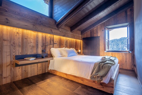 A wooden bedroom with a bed, a nightstand, and a window with a view of the outdoors. - HAUS PA 'SEFN "ACCOMMODATION" ON THE CLOUDS " (SAURIS)