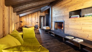 Une pièce chaleureuse avec un décor intérieur en bois, un canapé avec des coussins, une cheminée et des livres sur une étagère.