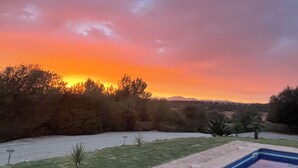 Ein Schwimmbecken mit Blick auf den Sonnenuntergang über einer hügeligen Landschaft.