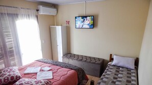 Ein Schlafzimmer mit zwei Betten, einem Fernseher, einem Kleiderschrank und einem Fenster mit Jalousien.