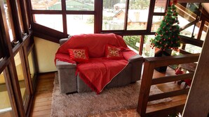 Ein gemütliches Zimmer mit einem grauen Sofa, roter Decke und einem Weihnachtsbaum.