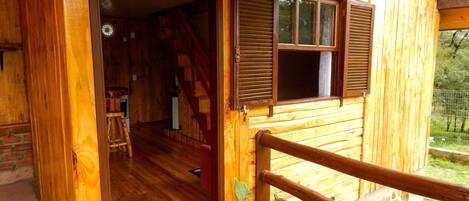 A wooden cabin with a wooden deck, a staircase leading to an upper level, and a potted plant on the deck.