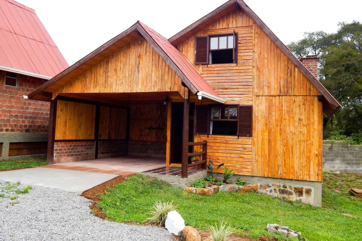 Una casa de madera con porche cubierto, paredes de ladrillo y techo rojo.