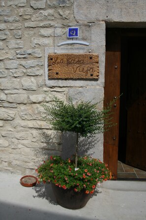 Un muro de piedra con una puerta de madera, un letrero que dice "La Casa de la Vida" y una planta en maceta con flores rojas.