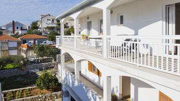 A white two-story building with a balcony, outdoor seating, and potted plants.