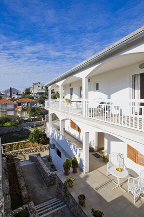 A white two-story building with a balcony, outdoor seating, and potted plants. - Guest House Kovacevic (Hvar)