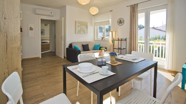 A dining area with a table set for two, a sofa in the background, and a view of the outdoors through a sliding door. - Guest House Kovacevic (Hvar)