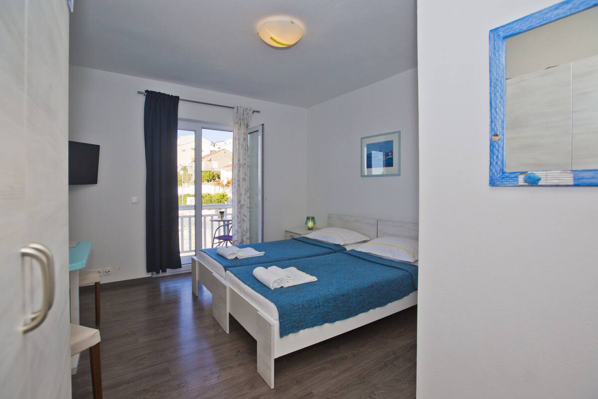 A bedroom with a bed, a chair, a desk, a TV, and a window with curtains.