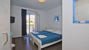 A bedroom with a bed, a chair, a desk, a TV, and a window with curtains.