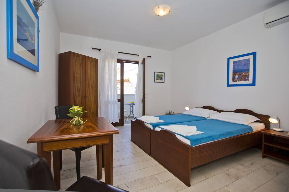 A bedroom with a wooden bed, a wooden desk, a chair, and a small table with a vase of flowers.