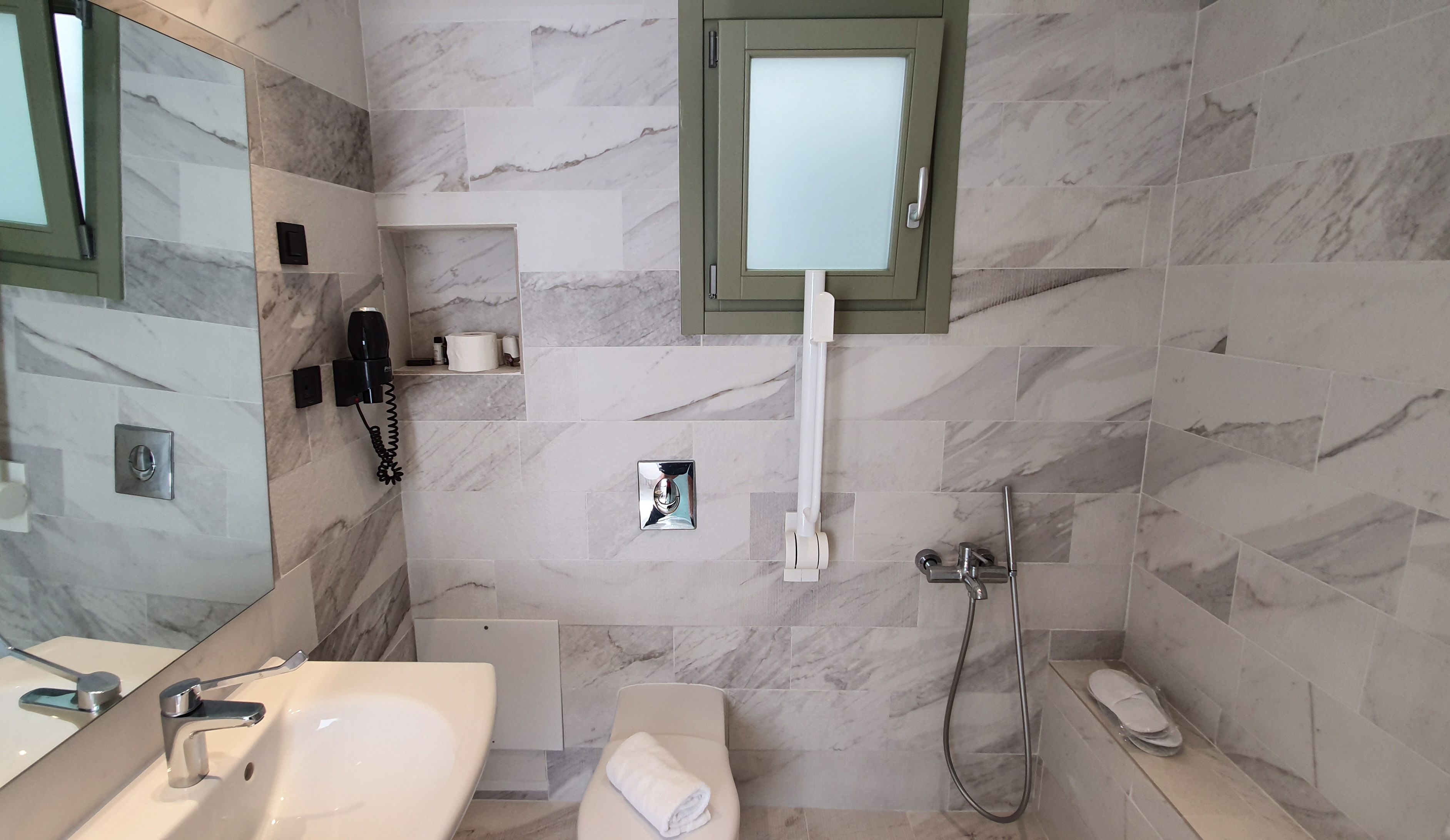 Un baño moderno con pared de mármol, inodoro integrado, lavamanos, espejo, ducha y toallero.