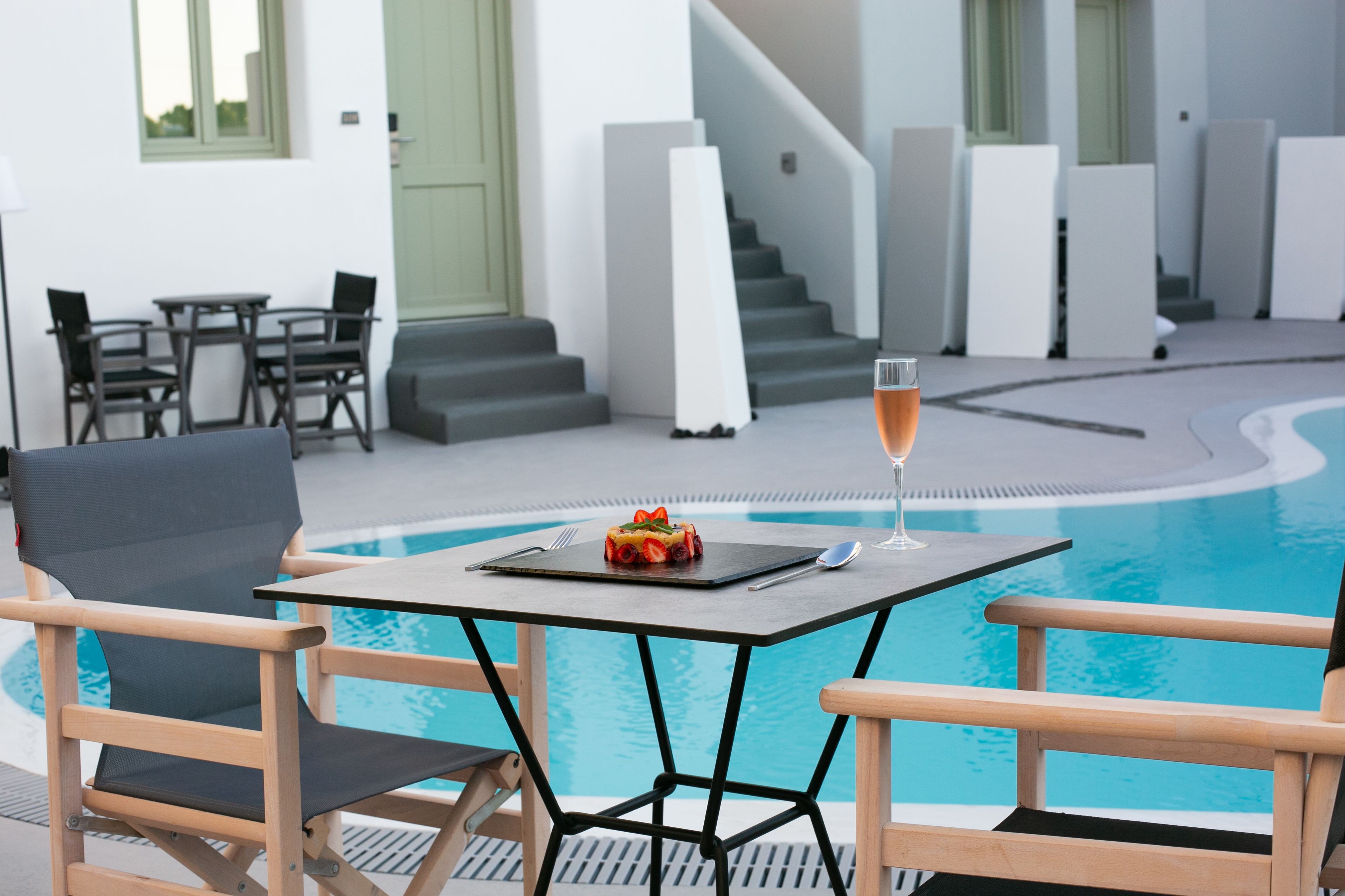 Un espace aménagé au bord de la piscine, avec une table, des chaises et une coupe de champagne.