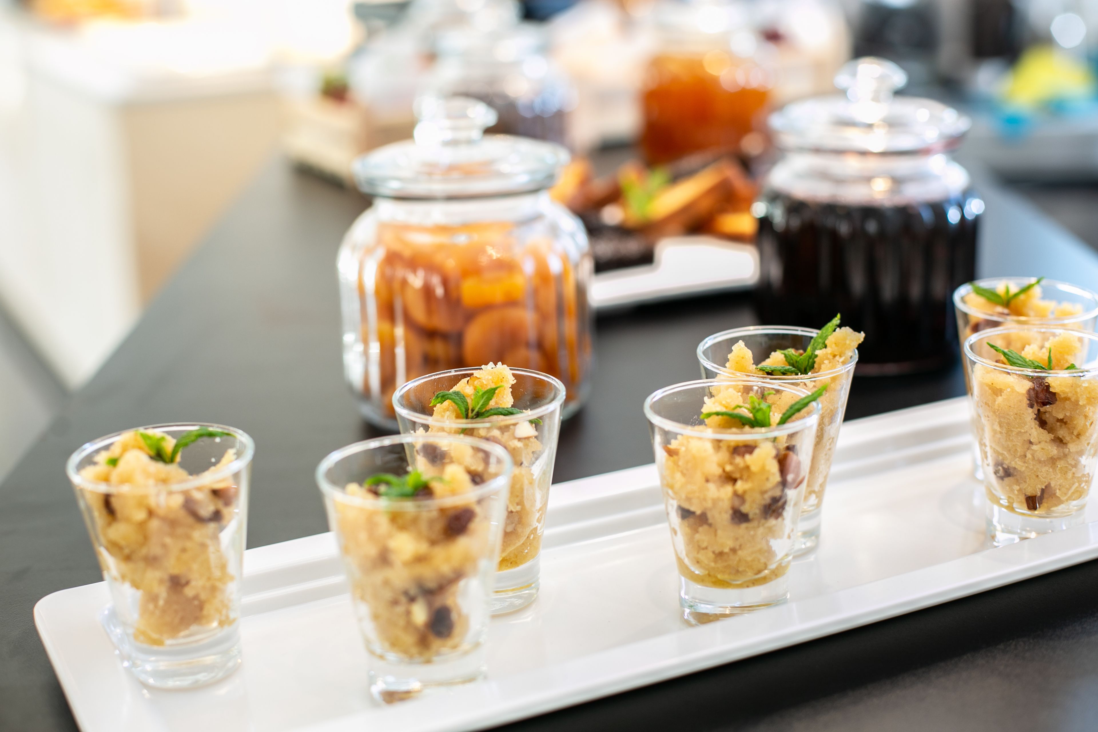 Una bandeja de pequeños postres con un dispensador de bebidas al fondo.