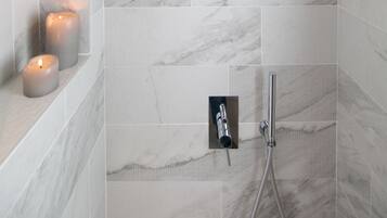 Una ducha moderna con cabezal de ducha de mano, grifo empotrado en la pared y una zona de ducha revestida con azulejos que imitan el mármol.
